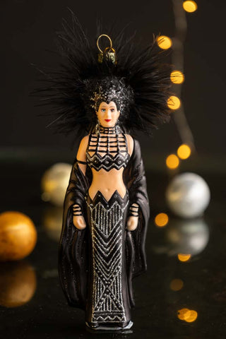 The Cher Inspired Christmas Tree Decoration displayed on a dark surface with baubles and fairy lights in the background.