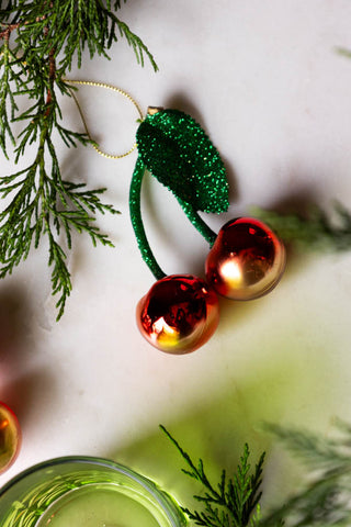 Cherries Christmas Tree Decoration on white marble with greenery closeup