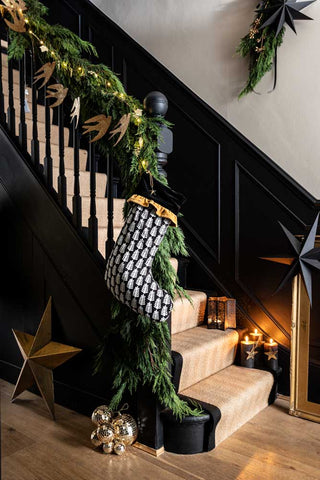 A Lifestyle image of The Luxury Christmas Tree Stocking hanging from some stairs with garlands, with some candles on the stairs in the background.