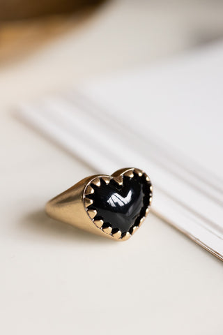 The Chunky Gold & Black Heart Ring styled on some paper.