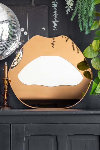 The Copper Pink Lips Decorative Mirror styled on a black sideboard with plants, a disco ball and a candlestick.