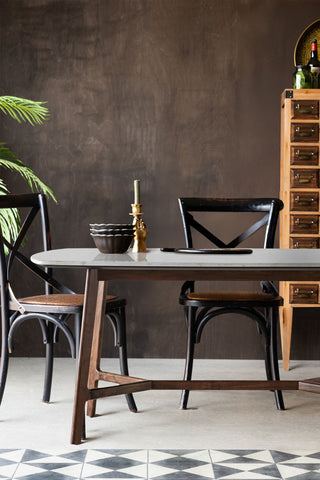 The Curved Acacia & Marble Dining Table in a room with a plant, storage unit and dining chairs, styled with some accessories on.