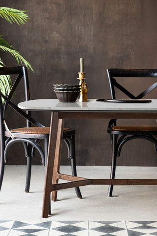 The Curved Acacia & Marble Dining Table styled with some accessories on, with some black dining chairs, a plant and a storage unit.