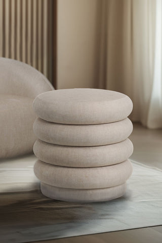 The Curved Cream Snug Footstool styled in a rug in a neutral living room.