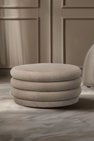 The Curved Cream Snug Ottoman styled in a living room next to an armchair.