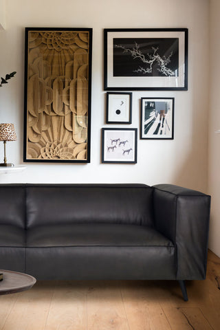 Close shot of the Dark Grey 3-Seater Leather Sofa styled in a living room in front of a wall decorated with art prints.