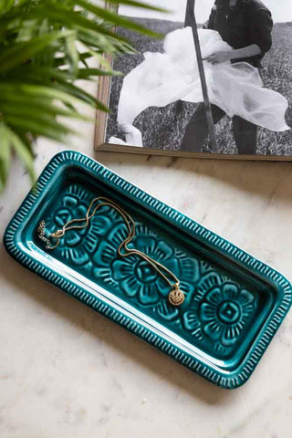 The Deep Blue Enamel Cast Style Trinket Tray displayed on a marble table with a necklace inside, styled with a plant and a book.