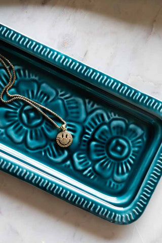 The Deep Blue Enamel Cast Style Trinket Tray displayed on a table with a necklace inside.