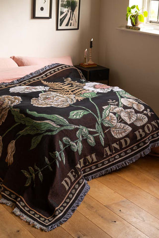 The Denim & Bone Scandi Black Woven Cotton Throw styled across a bed in a bedroom, with various home accessories and a plant.