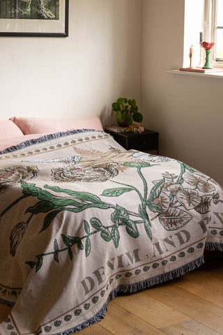 The Denim & Bone Scandi White Woven Cotton Throw styled on a bed in a white bedroom, styled with a plant and various home accessories.