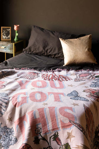 The Denim & Bone You Got This Woven Cotton Throw styled on the corner of a bed in a dark bedroom.