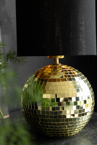 Close-up of the base of the Disco Ball Table Lamp in Gold styled on a dark surface with a plant.