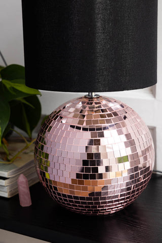 Close-up of the base of the Disco Ball Table Lamp in Pink, styled with a crystal, a plant and some magazines.