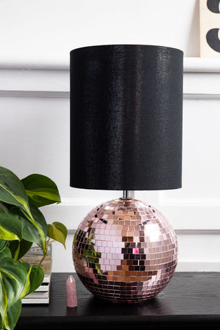 The Disco Ball Table Lamp in Pink styled on a dark surface with a pink crystal, a plant and some magazines.