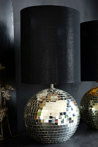 The Disco Ball Table Lamp in Silver styled on a dark mantle piece and wall