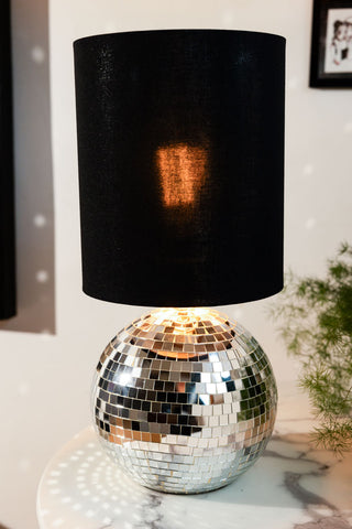 The Disco Ball Table Lamp in Silver switched on, styled on a white marble table next to a plant.