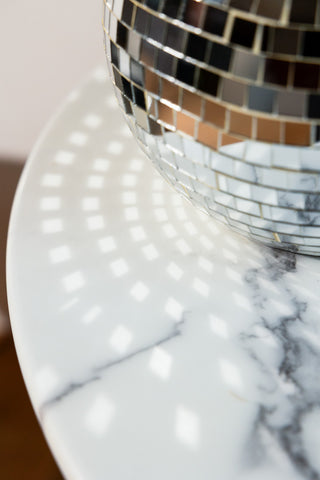 Close-up of the Disco Ball Table Lamp in Silver, reflecting light onto the marble table it is displayed on.