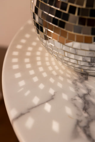 Close-up of the Disco Ball Table Lamp in Silver, reflecting light onto the marble table it is displayed on.