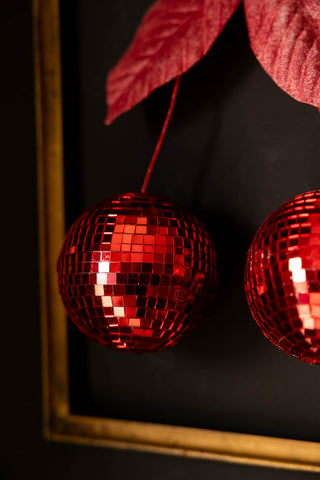 Close-up of the Disco Cherries Christmas Tree Decoration hanging on a dark wall inside a frame.