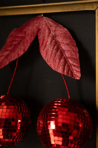 Close-up of the leaves on the Disco Cherries Christmas Tree Decoration, styled hanging on a dark wall in a frame.