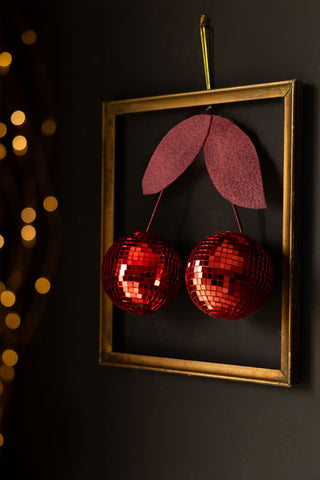 Image of the Disco Cherries Christmas Tree Decoration styled hung on the wall in a gold frame.