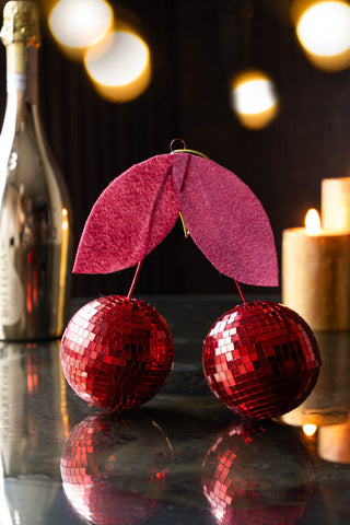 Disco Cherries Christmas Tree Decoration on glass table with candles and gold bottle in background