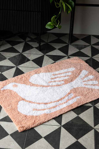 Shot of the Dove Tufted Cotton Bath Mat styled on a geometric patterned floor, with a cupboard and plant in the background.