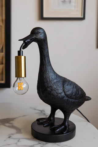 The Duck Table Lamp styled on a table with artwork on the wall in the background.