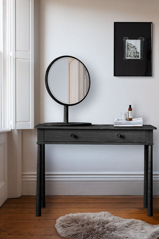 The Elegant Black Dressing Table in front of a white wall next to a window, styled with various accessories on.