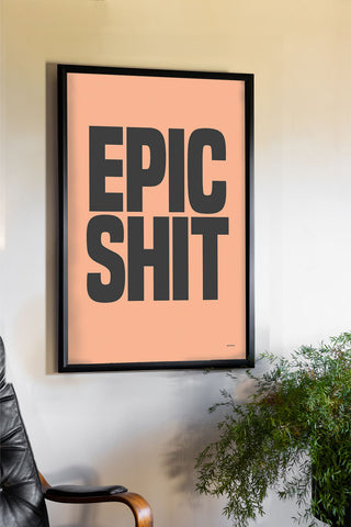 The Epic Shit Coral & Black Art Print - Unframed styled in a black frame, displayed on a neutral wall above a desk chair and a plant.