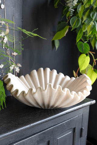 A large bowl in a shell design styled on a black sideboard surrounded by greenery.