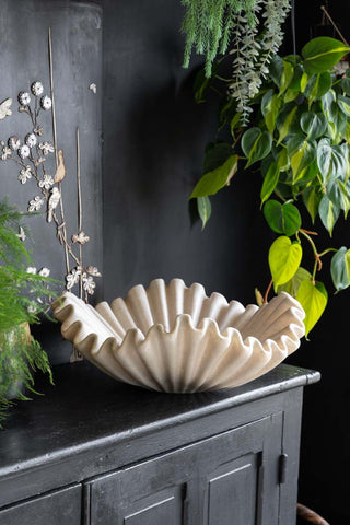 A large shell design bowl displayed on the corner of a black sideboard, surrounded by lots of greenery.