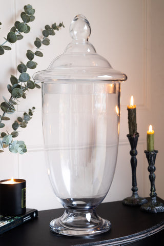 Extra-large glass apothecary jar with a rounded lid, styled on a black table with candles and eucalyptus sprigs in the background.