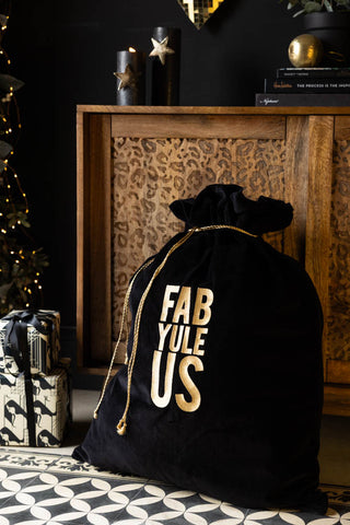 The Fab Yule Us Velvet Christmas Sack styled with some presents in front of a leopard print unit and a Christmas tree, styled with various decorative home accessories.