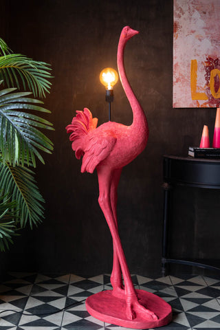 The Fabulous Pink Ostrich Floor Lamp switched on and styled next to a plant, table, artwork and home accessories.