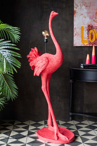 The Fabulous Pink Ostrich Floor Lamp displayed on a geometric floor, next to a large plant, console table with accessories on and some wall art.