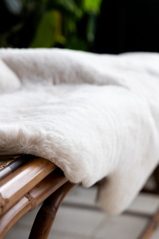 Close-up of the Faux Fur Natural Rug displayed on a wicker bench.