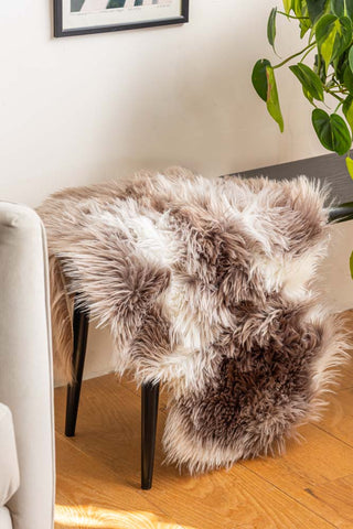 The Faux Sheepskin Rug in White & Walnut draped over a bench, styled next to a chair, plant and art print.