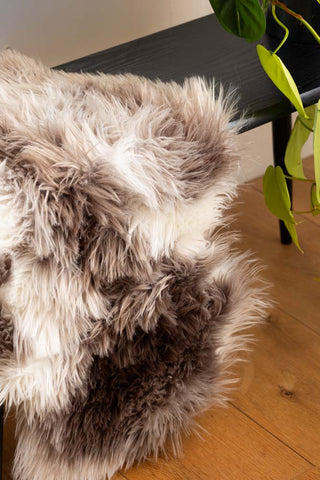 Close-up of the Faux Sheepskin Rug in White & Walnut on a bench, styled next to a plant.