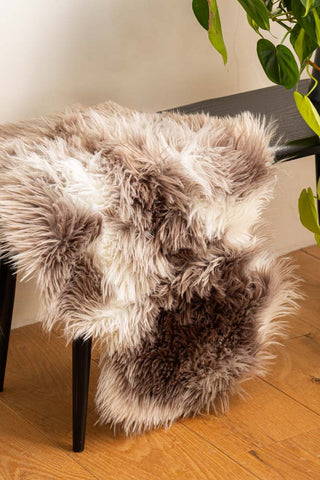 The Faux Sheepskin Rug in White & Walnut draped across a bench, next to a plant.