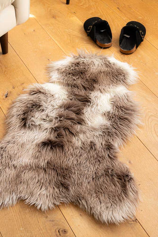 The Faux Sheepskin Rug in White & Walnut on a wooden floor, styled with a sofa and some shoes in the background.