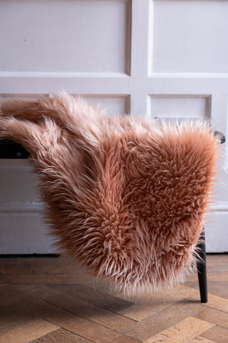 The Faux Sheepskin in Blush displayed on a black bench.