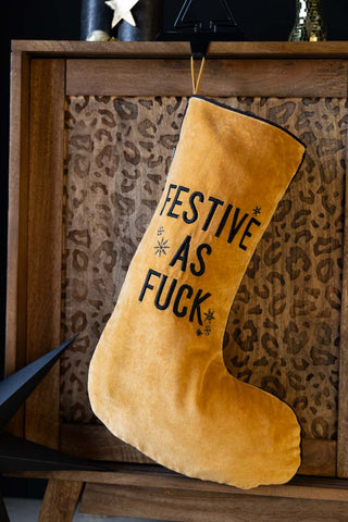 The Festive As Fuck Gold Christmas Stocking hanging in front of a wooden leopard print unit, styled with Christmas decorations.