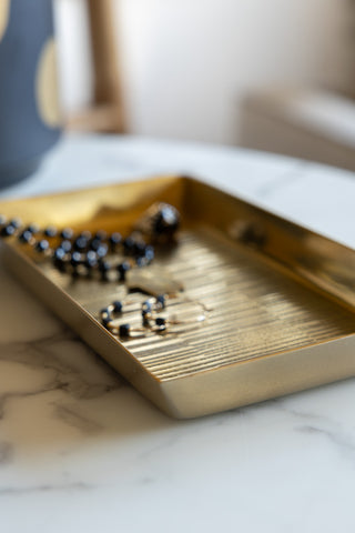 Detail shot of the corner of the Fine Line Detail Gold Effect Trinket Tray styled with some jewellery inside.