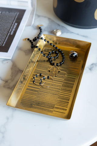 The Fine Line Detail Gold Effect Trinket Tray styled with various pieces of jewellery on, displayed on a white marble table.