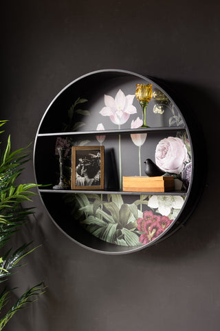 A round floral shelf styled on the wall, with various home accessories and a large plant.