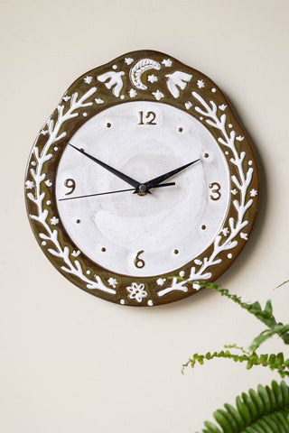 The Folk Birds Ceramic Clock displayed on a neutral wall, with a plant in the corner of the shot.