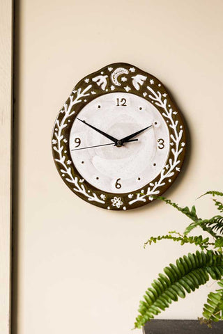 The Folk Birds Ceramic Clock on a wall, styled with a plant.