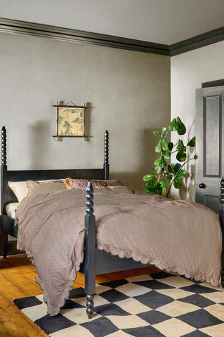 The Folk Bobbin Bed styled in a bedroom with a patterned rug, plant and wall art.