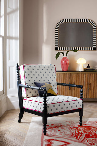 The Folk Bobbin Chair styled with a cushion on, displayed on a rug by a window, with a sideboard, mirror and various home accessories in the background.